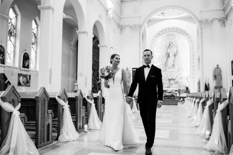 Jaunavedžiai eina bažnyčios nava po ceremonijos – juodai balta vestuvių nuotrauka, Birute Bras Photography