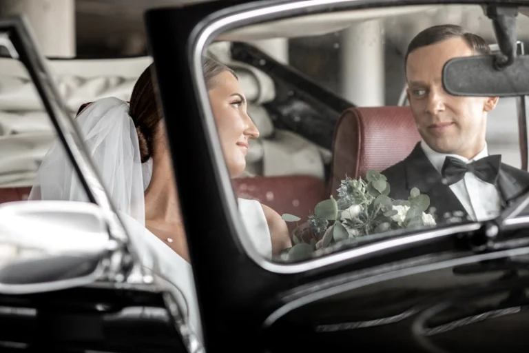 Nuotaka ir jaunikis žiūri vienas į kitą pro senovinio automobilio langą – romantiška vestuvių akimirka, Birute Bras Photography