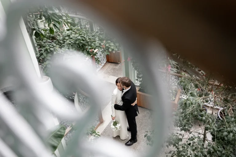 Pora apsikabinę šiltnamyje tarp egzotiškų augalų – romantiškas vestuvių portretas iš viršaus, Birute Bras Photography